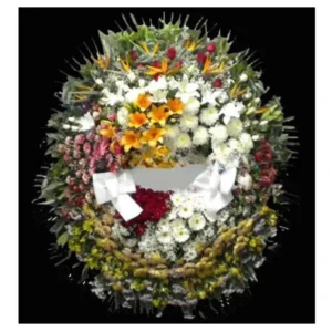 Arreglo fúnebre en forma de corona con flores multicolores y lazos blancos, ideal para ceremonias de despedida