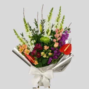 Ramo multicolor elegante con lirios blancos, alstroemerias rojas y rosadas, crisantemos verdes, statice púrpura y anthuriums rojos, envuelto en papel plateado con lazo blanco. Arreglo floral vertical para celebraciones y regalos.