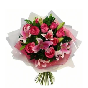 Ramo rosado con lirios y rosas frescas, envuelto en papel blanco y rosa con follaje verde. Ideal para celebraciones y regalos delicados.