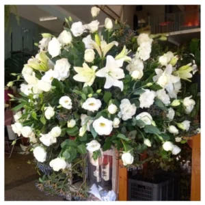 Centro Blanco Premium: arreglo floral simétrico con lirios y rosas blancas, acompañado de follaje verde, ideal para decoración elegante y eventos formales.