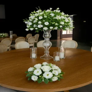 Centro alto blanco con rosas, lirios y lisianthus sobre jarrón de vidrio transparente, rodeado de velas blancas en portavelas cilíndricos. Arreglo floral vertical ideal para bodas y eventos formales.