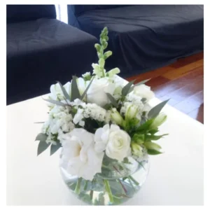 Centro floral blanco con rosas, lisianthus y alstroemerias en florero esférico de vidrio transparente, un diseño elegante y refinado ideal para decorar mesas, recepciones y espacios íntimos.