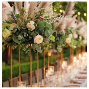 Centro mesa alto con rosas marfil, follaje verde y pampas sobre bases doradas, un diseño elegante y sofisticado ideal para bodas, recepciones y eventos especiales.