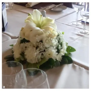 Centro mesa blanco con lirio, rosas y crisantemos en composición compacta y elegante con follaje verde, ideal para bodas, recepciones y celebraciones especiales.