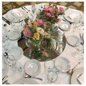 Centro mesa floral con rosas rosadas y durazno en jarrones de vidrio sobre base espejada, un diseño romántico y elegante ideal para recepciones, bodas y celebraciones especiales.