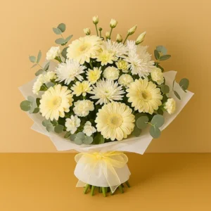 Ramo Luz Serena con gerberas amarillas suaves, crisantemos blancos, flores pequeñas, follaje de eucalipto, envoltura blanca con tul amarillo y lazo de organza, sobre fondo beige y mesa clara. Composición circular, luminosa y armoniosa.
