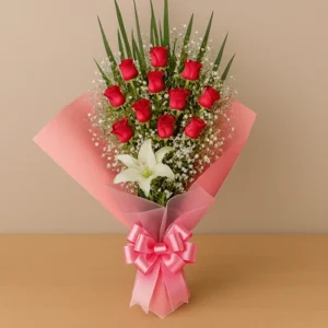 Ramo Rosas y Lirio con rosas rojas, lirio blanco, gypsophila, follaje verde, envoltura rosa y lazo satinado, sobre fondo beige y mesa clara. Composición vertical, elegante y armoniosa.