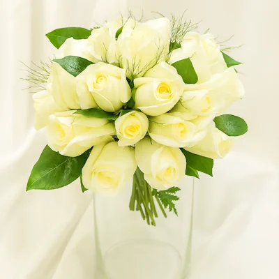Ramo de rosas blancas redondo, compacto y elegante, adornado con follaje verde y ramitas decorativas, presentado en florero de vidrio transparente. Arreglo ideal para novias y ocasiones especiales.