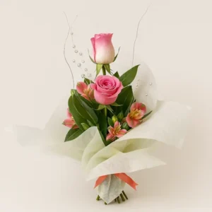 Ramo Rosa Encanto con rosas rosadas, alstroemerias y follaje verde, envuelto en papel blanco con lazo rojo y detalles decorativos plateados, sobre fondo claro. Composición vertical, elegante y equilibrada.